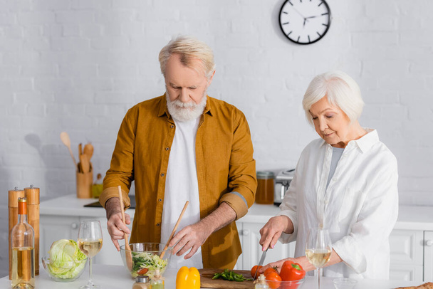 Senior couple cooking salad near wine in kitchen  - Photo, Image
