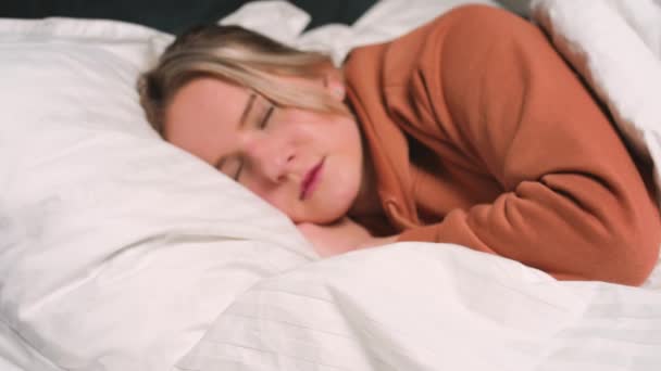 Close-up portret van ontspannen vrouw slapen op een wit kussen in bed. Portret van een jonge blanke vrouw die thuis in de slaapkamer rust. Vrije tijd en ontspanning. - Video