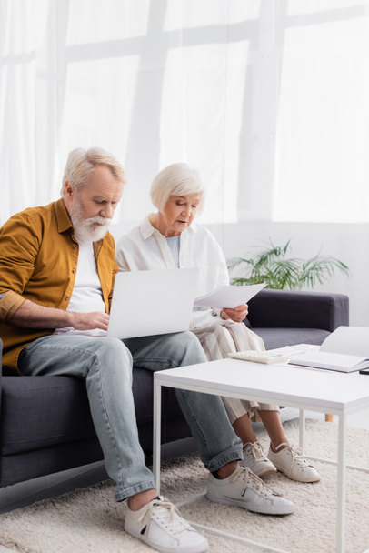Elderly couple with laptop and papers sitting on couch  - Photo, Image