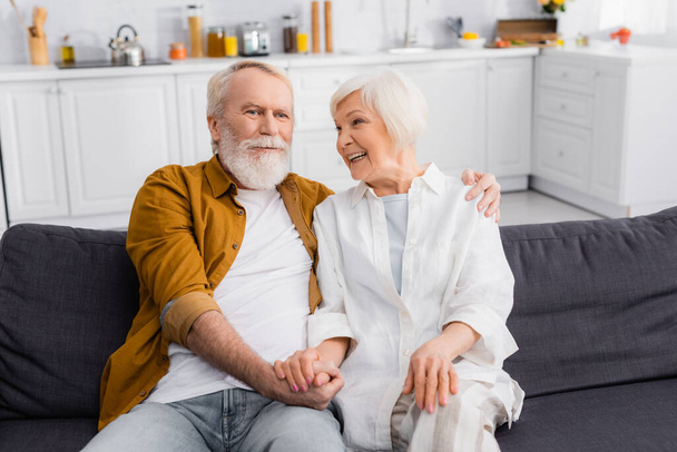 Ηλικιωμένο ζευγάρι αγκαλιάζει και κρατά τα χέρια στον καναπέ  - Φωτογραφία, εικόνα
