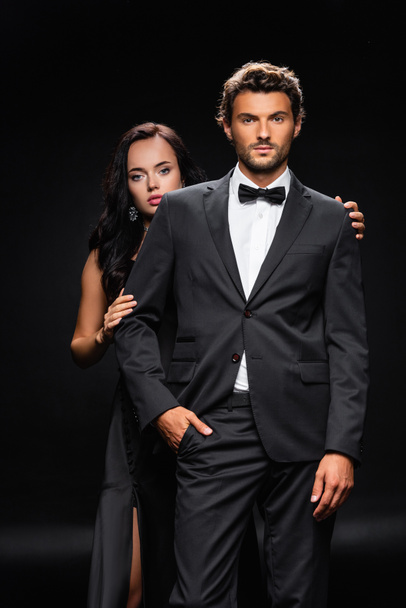 young confident man with hand in pocket near sensual brunette woman on black - Photo, Image