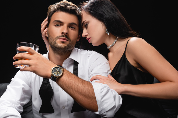 férfi üveg whiskey nézi kamera közelében szexi nő átöleli őt elszigetelt fekete - Fotó, kép