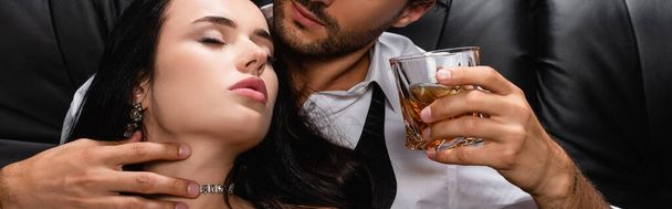 muž drží sklenici whisky při objímání krku smyslné ženy, prapor - Fotografie, Obrázek