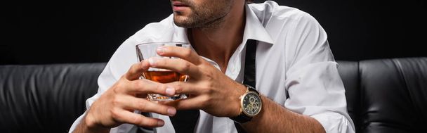 przycięty widok człowieka w białej koszuli i rozwiązany krawat trzymając szklankę whisky izolowane na czarno, baner - Zdjęcie, obraz