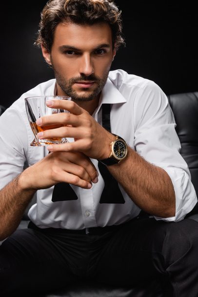 man in white shirt and untied tie holding glass of whiskey and looking at camera isolated on black - Zdjęcie, obraz
