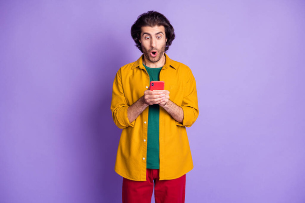 Photo of young shocked excited astonished man male guy look unbelievable news information in phone isolated on purple color background - Photo, image