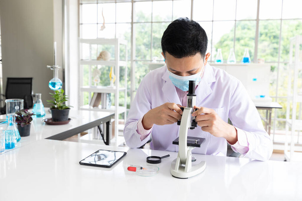 hombre de ciencia que usa mascarilla médica para proteger el virus y usar microscopios en el laboratorio - Foto, imagen