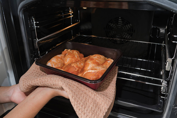 Το κορίτσι βάζει το ψητό κοτόπουλο στη συσκευασία του φούρνου στο φούρνο. - Φωτογραφία, εικόνα