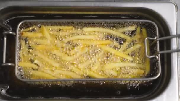 Tasty french fries is cooking into deep fryer at kitchen. Crispy potatoes is frying in hot boiling oil at cuisine. Process of making fast food. Concept of preparing food. Top view Slow motion - Footage, Video