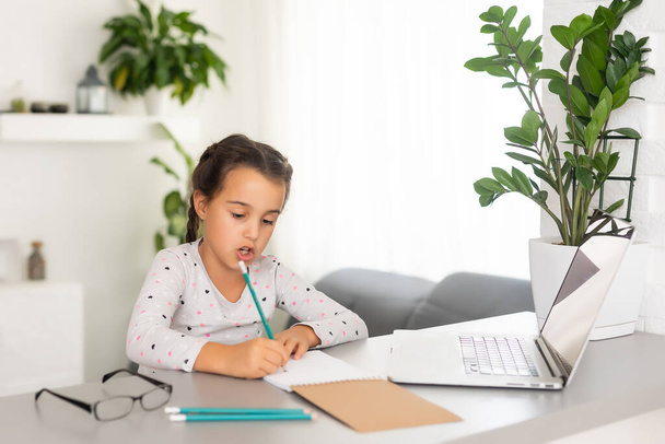 Little girl studying online using her laptop at home - Fotó, kép