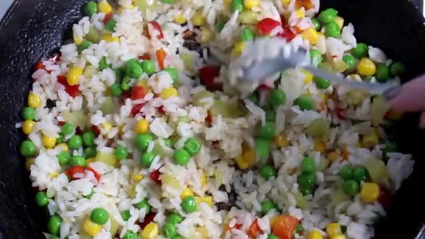 Bevroren groentemengsel met rijst in een koekenpan, die met een lepel wordt geroerd. Het uitzicht vanaf de top. - Video