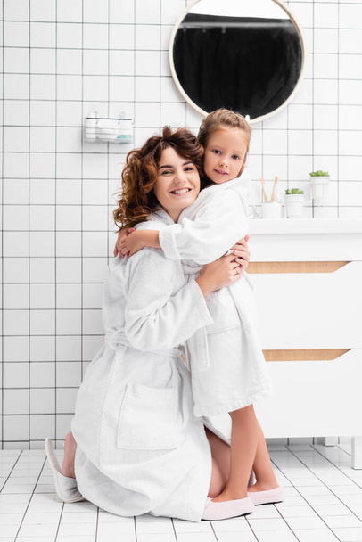 Daughter and mother in bathrobes hugging in bathroom  - Foto, Imagen
