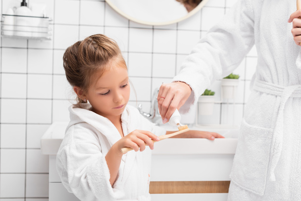 Mother squeezing toothpaste on brush near daughter in bathroom  - Foto, immagini