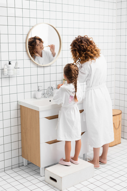 Woman and child brushing teeth near mirror and sink in bathroom  - Fotoğraf, Görsel