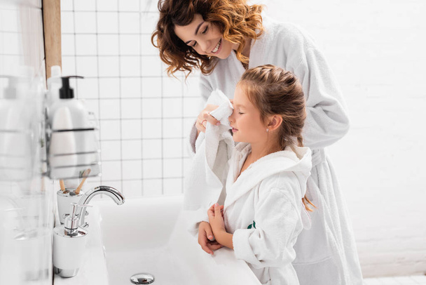 Madre sorridente asciugandosi la faccia di figlia con asciugamano in bagno  - Foto, immagini