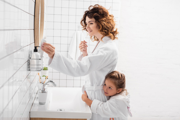 Smiling woman taking toothpaste near child in bathroom  - Valokuva, kuva