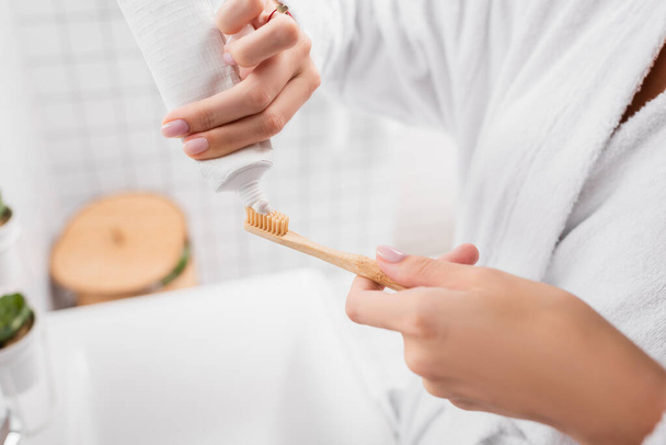 Cropped view of woman applying toothpaste on toothbrush in bathroom  - Фото, зображення