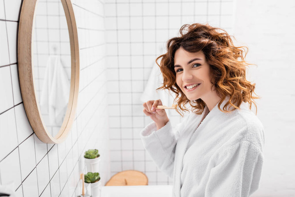 Smiling woman holding toothbrush near mirror and looking at camera  - Foto, immagini