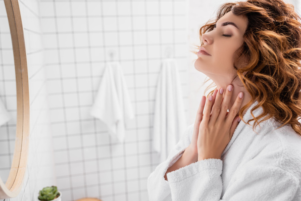 Curly woman with hands near neck standing in bathroom  - Foto, Imagem