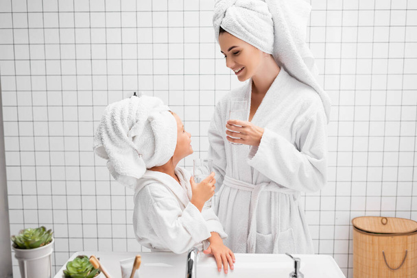Anne ve kızı modern banyoda su bardakları tutuyorlar.  - Fotoğraf, Görsel