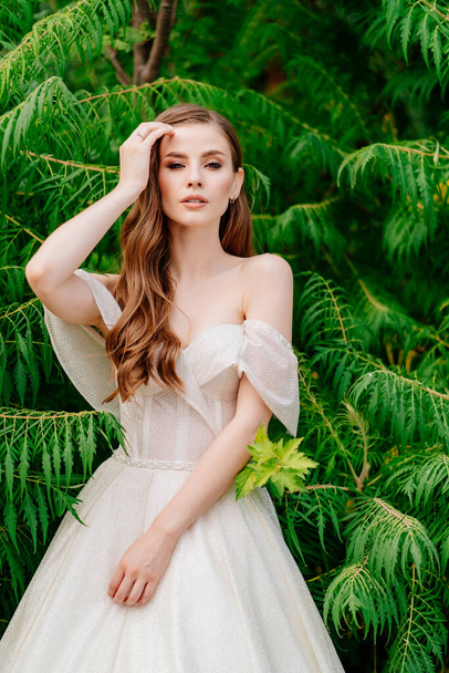 beautiful woman in a white dress posing in against of green leaves. - Foto, imagen