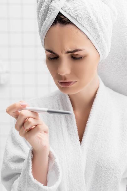 Soustředěná žena s ručníkem na hlavě při pohledu na těhotenský test  - Fotografie, Obrázek