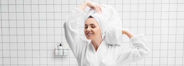 Mulher sorridente em roupão de banho e toalha de pé com olhos fechados no banheiro, banner  - Foto, Imagem
