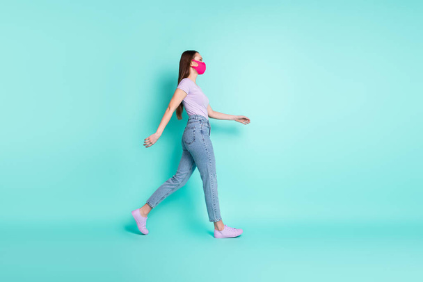 Full length body size side profile portrait of girl wearing pink respiratory mask going fast isolated on vibrant teal color background - Фото, изображение
