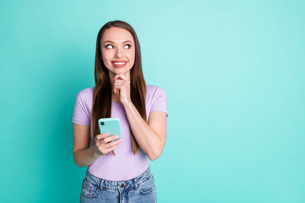 Retrato fotográfico de una niña reflexiva usando un teléfono inteligente mirando el espacio vacío sonriendo aislado sobre un vibrante fondo de color verde azulado - Foto, Imagen