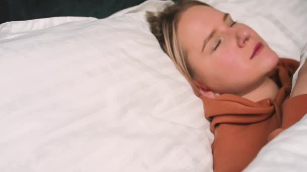 Nahaufnahme Porträt einer entspannten Frau, die auf einem weißen Kissen im Bett schläft. Porträt einer jungen Kaukasierin, die zu Hause im Schlafzimmer ruht. Freizeit und Entspannung. - Filmmaterial, Video