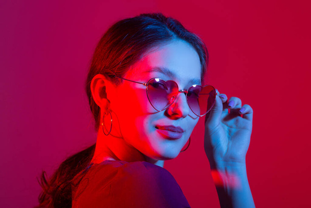 portrait of a beautiful young woman with colored lighting in sunglasses - 写真・画像