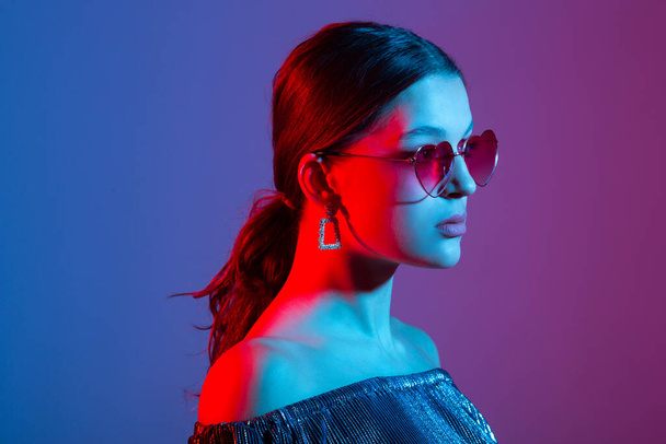portrait of a beautiful young woman with colored lighting in sunglasses - Foto, Imagem