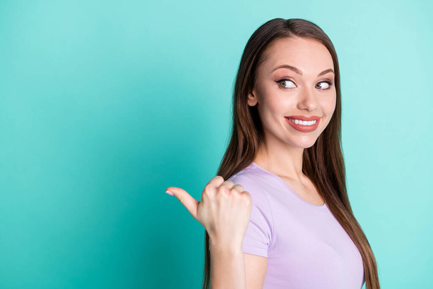 Side profile photo of girl pointing at copyspace with thumb smiling isolated on vivid teal color background - Фото, зображення