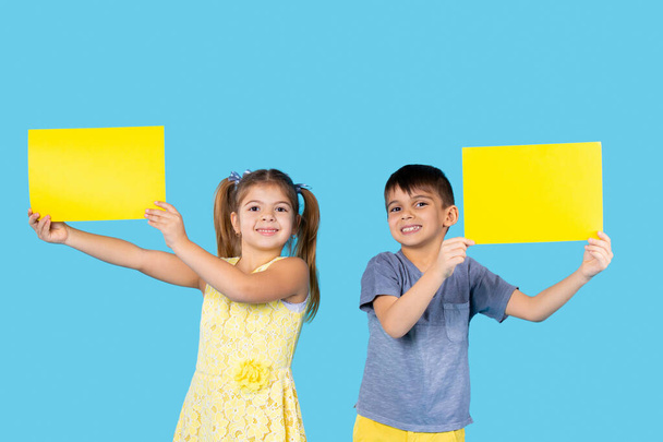 Preschool kids posing with yellow letterhead for your advertisement. Photo on a blue background. - Foto, immagini