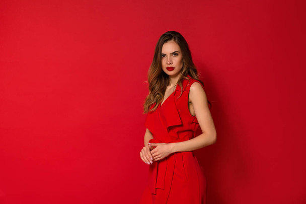 Уверенная в себе стильная волнистая женщина в хорошем настроении в вечернем платье, позируя на красном изолированном фоне - Фото, изображение