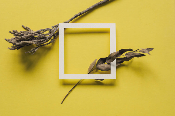 Minimal flat lay with simple white frame and leaves on bright yellow backdrop. Trendy color of the year 2021. Hipster style composition. Vivid banner template with copy space. - Photo, Image