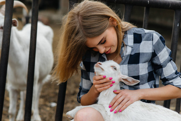 A young pretty girl poses on a ranch with goats and other animals. Agriculture, livestock breeding - Fotografie, Obrázek