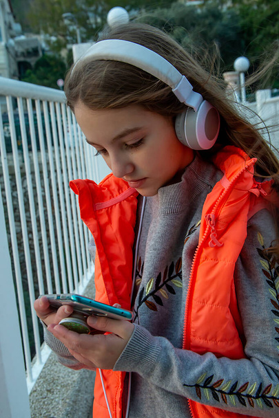 teenage girl in headphones and bright orange vest against the background of the city - Φωτογραφία, εικόνα