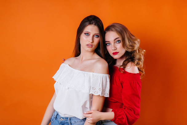 Two young and beautiful girls shows emotions and smiles in the Studio on an orange background. Girls for advertising - 写真・画像