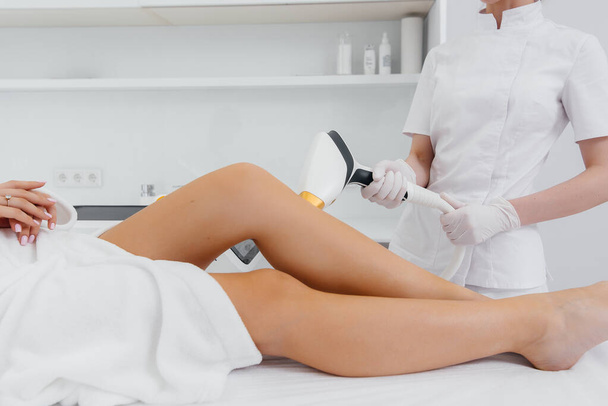 A beautiful young girl will perform a laser hair removal procedure with modern equipment in the Spa salon close-up. Beauty salon. Body care - Photo, image