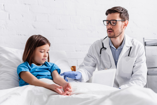gyermekorvos digitális tabletta beszél gyermek ül az ágyon a kórházban - Fotó, kép