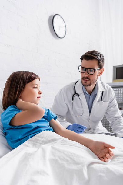 sick girl in bed touching neck near pediatrician in hospital - Фото, зображення