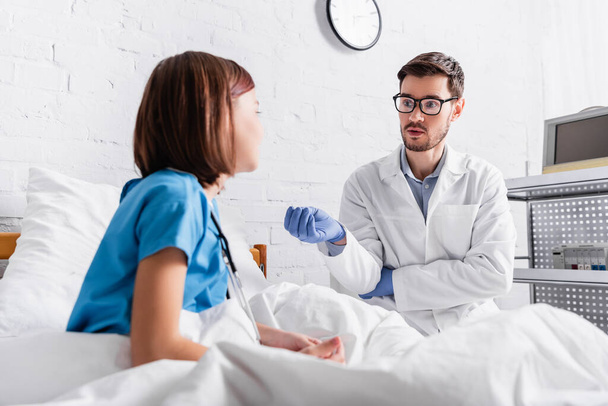 pediatrician in latex gloves gesturing while talking to child on blurred foreground - Foto, Imagem