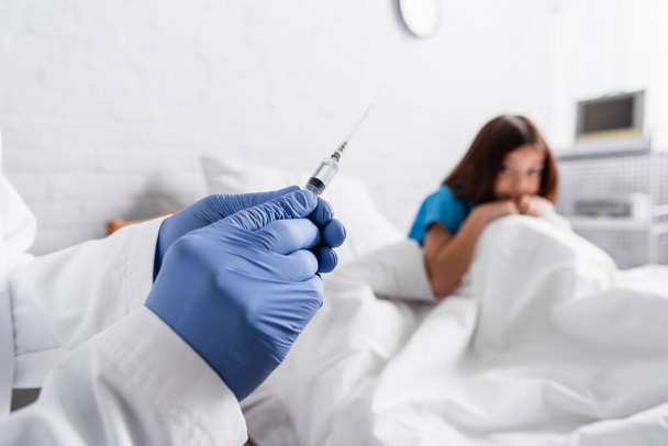 criança com medo sentada na cama perto do médico com a seringa em primeiro plano turvo - Foto, Imagem