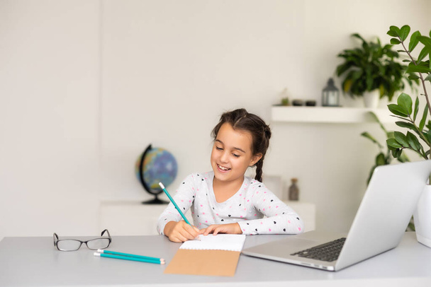 Evde bilgisayarını kullanarak internetten ders çalışan küçük bir kız. - Fotoğraf, Görsel