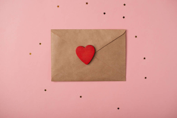 Craft envelope with the red heart and little golden stars on the rose background. Flat lay, top view. Romantic love letter for Valentine's day concept. - Photo, image
