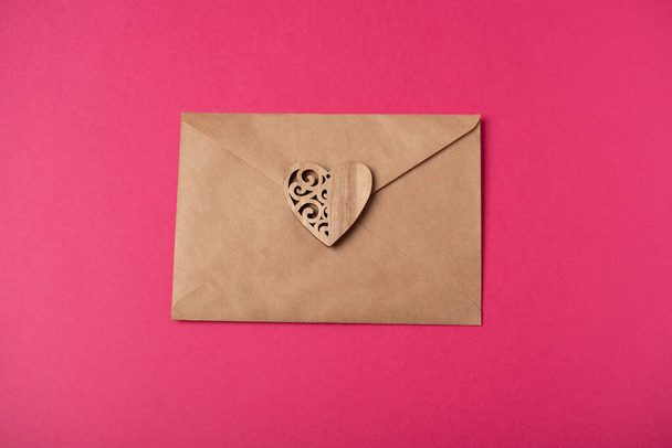 Craft envelope with the wooden heart on the hot pink background. Flat lay, top view. Romantic love letter for Valentine's day concept. - Photo, image