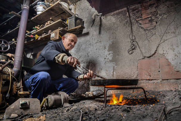 Idős ember a műhelyében lemezeket réz tál ón. Tinsmith borító réz tárgy ón a tűz felett - Fotó, kép
