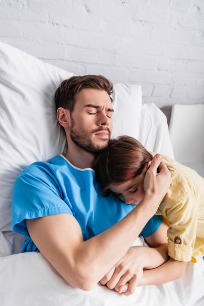 beteg férfi átöleli lánya, miközben feküdt a kórházi ágyban csukott szemmel - Fotó, kép