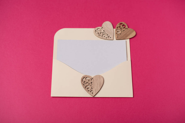 Envelope with a blank sheet of paper inside and wooden hearts on the hot pink background. Romantic love letter for the Valentine's day concept. Space for text. - Foto, Bild